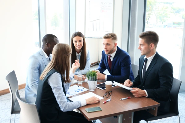 young-handsome-man-gesturing-discussing-something-while-his-coworkers-listening-him-sitting-office-table